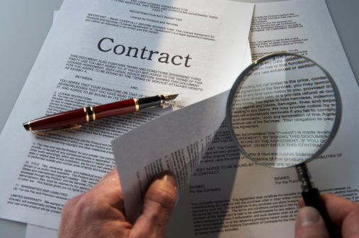 Man's hands examining small print of contract with magnifying glass